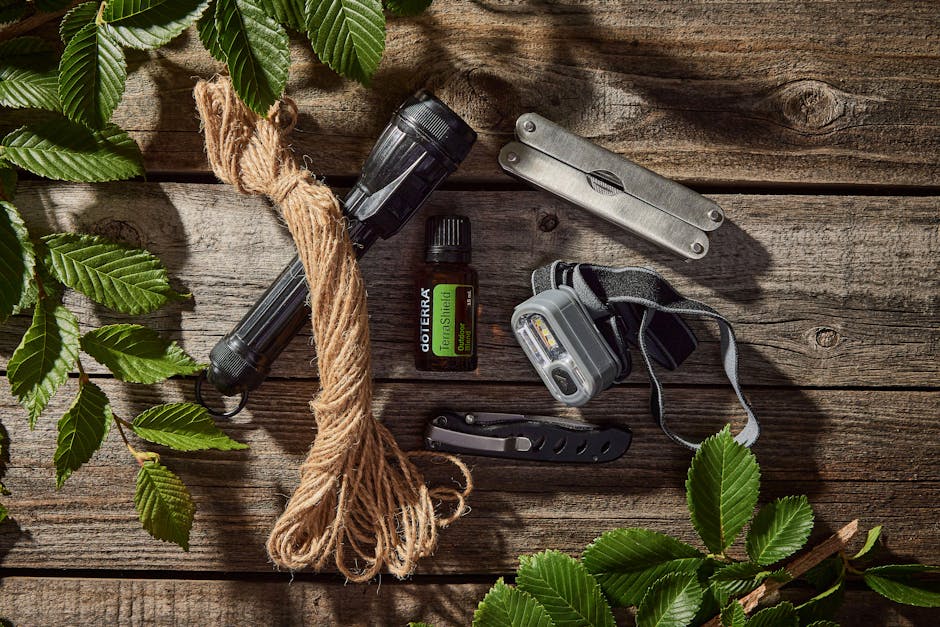 Collection of outdoor essentials including flashlights, rope, pocket knife, and essential oil on a wooden surface.
